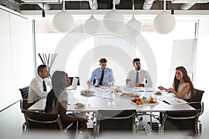 Businessmen And Businesswomen Meeting In Modern Boardroom Over Working Lunch