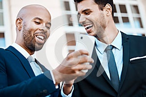 Businessmen can have banter too. young handsome businessmen using a cellphone together outside.