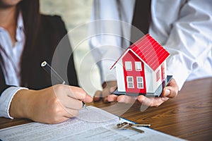 Businessmen and customers are signing home purchase agreements. Hand holding the pen signing purchase contract. Gray roof houses