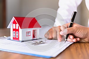 Businessmen and customers are signing home purchase agreements. Hand holding the pen signing purchase contract. Gray roof houses
