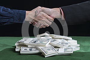 The businessmen going to shake hands against pile of dollars