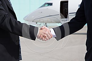 Businessmen handshake in front of a corporate jet