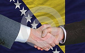 businessmen handshake after good deal in front of bosnia herzegovina flag