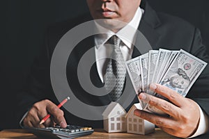 Businessmen hold dollar bills and use calculator to calculate home loan installments