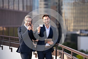 Businessmen holding credit card while paying online via tablet. Two business men in suit hold credit card and laptop