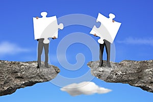 Businessmen holding jigsaw puzzles to connect on cliff with sky