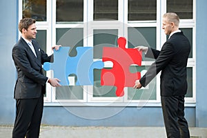 Businessmen Joining Jigsaw Pieces Outside Office