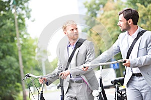 Businessmen looking at each other while holding bicycles outdoors