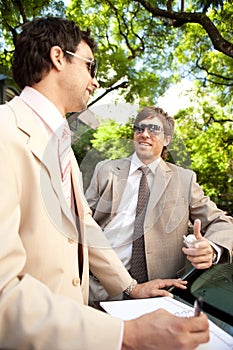 Businessmen meeting around car.