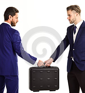 Businessmen with serious faces hold black briefcase.