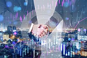 Businessmen shaking hands on blurry bokeh night city background with candlestick forex chart. Teamwork, success and partnership