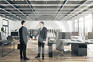 Businessmen shaking hands in modern concrete and wooden coworking office interior with furniture, equipment and window with city