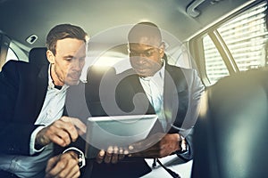 Businessmen sitting in the backseat of a car working online