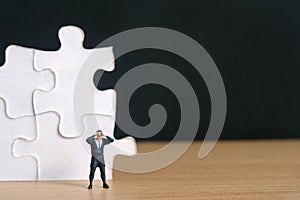 Businessmen standing in front of jigsaw puzzle piece stack using binoculars on wooden table. Miniature tiny people toys