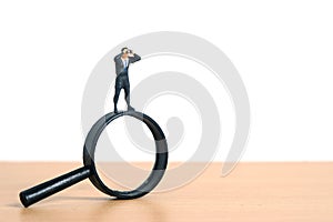 Businessmen standing using binoculars above magnifying glass. Miniature tiny people toys photography. isolated on white background