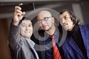 Businessmen in suits doing selfie indoors, mature. Business team of three people. Modern technology, social networking