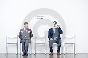 Businessmen in suits sitting on chairs at white waiting room