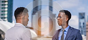 businessmen talk together, building in city and light at background. black man in grey suit and executive man with glasses in blue