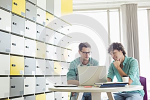 Businessmen using laptop at table in locker room at creative office