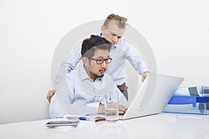 Businessmen using laptop together at desk in office