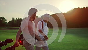 Businessmen walking golf course outside. Two players carry clubs in sportswear.