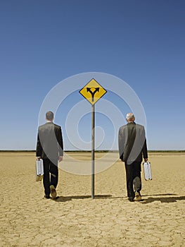 Businessmen Walking Past Road Sign In Desert