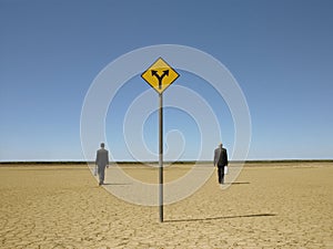 Businessmen Walking Past Road Sign In Desert