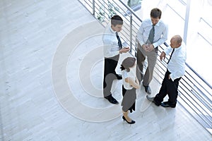 Businessmen and woman standing together by railing and conversing