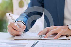 Businessmen writes in notebook while sitting white desk.Businessman hand holding pen writing book