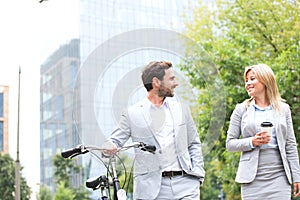 Businesspeople with bicycle and disposable cup conversing while walking outdoors