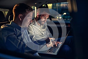 Businesspeople in car working on laptop in back seat