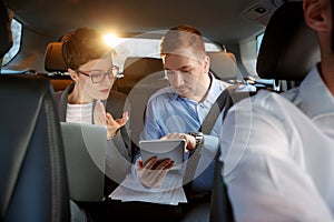Businesspeople with computer and tablet in car on trip