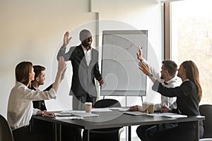 Businesspeople led by African coach raising hands engaged in voting