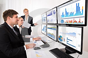Businesspeople Looking At Financial Graphs On Multiple Computer