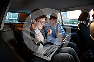 Businesspeople looking at laptop in car on trip