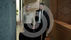 Businesspeople man and woman leaving hotel with luggage walking in lobby talking