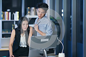 Businesspeople in the office at night working late, Two young businesspeople working overtime together over a laptop at a desk in