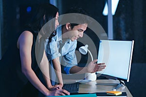 Businesspeople in the office at night working late, Two young businesspeople working overtime together over a laptop at a desk in