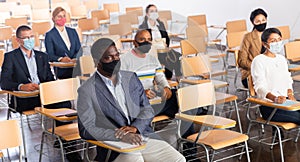 Businesspeople in protective masks listening to presentation in conference room