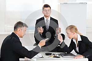 Businesspeople Quarreling In Front Of Businessman Meditating