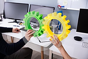 Businesspeople`s Hand Joining Green And Yellow Gears