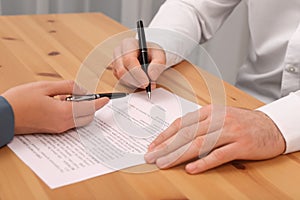 Businesspeople signing contract at wooden table in office, closeup of hands