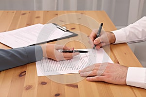 Businesspeople signing contract at wooden table in office, closeup of hands