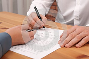 Businesspeople signing contract at wooden table in office, closeup of hands