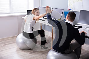 Businesspeople Sitting On Fitness Ball Giving High Five