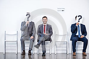 Businesspeople sitting in queue and waiting for interview, holding question marks in office