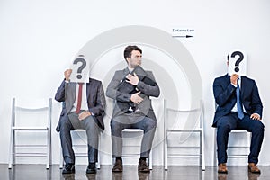 Businesspeople sitting in queue and waiting for interview, holding question marks in office