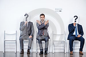 Businesspeople sitting in queue and waiting for interview, holding question marks in office