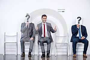 Businesspeople sitting in queue and waiting for interview, holding question marks in office