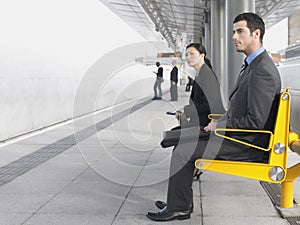 Businesspeople Sitting On Train Station Bench